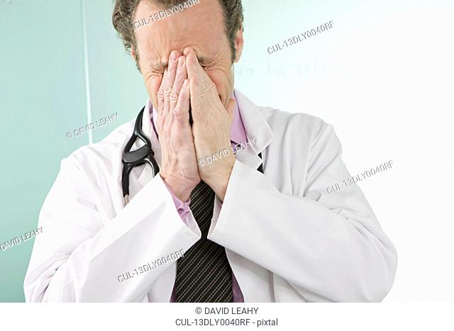 A doctor holding his hands over his face