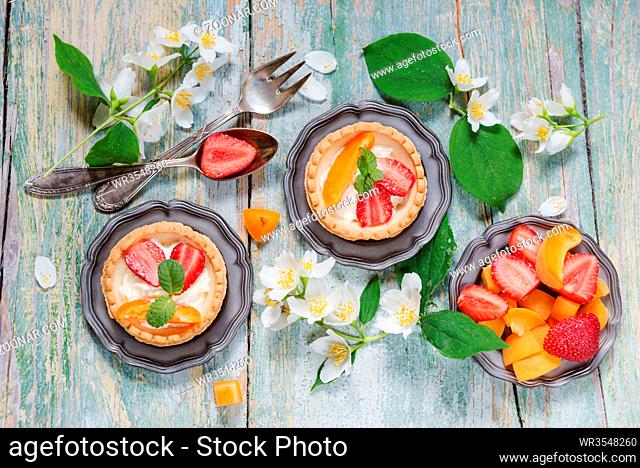 Still life with tartlets filled with cream and berries and jasmine flowers on old shabby boards, top view