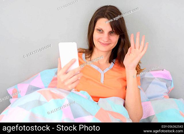 Girl lying in bed waving her hand while chatting via video calling