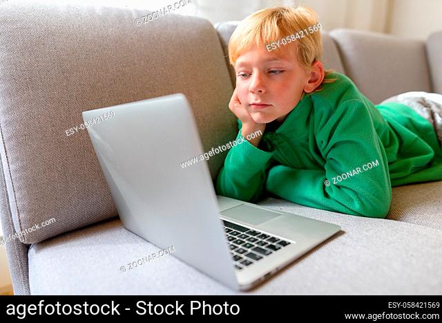 Portrait of young handsome boy with blond hair sitting on the couch in the living room at home