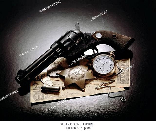 Close-up of an antique handgun with a badge, pocket watch and bullets