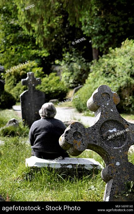 Woman sitting near medieval stone cross of the Glendalough monastery in the Wicklow mountains in Ireland