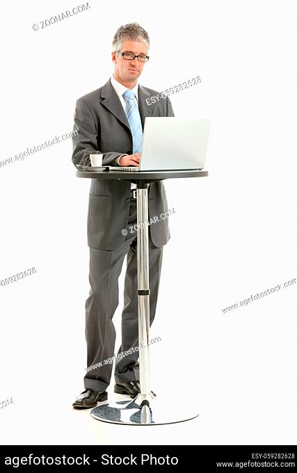 Businessman standing at coffee table, using laptop computer, looking at screen. Isolated on white