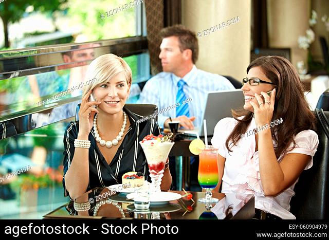 Young women sitting in cafe having sweets, talking on mobile phone
