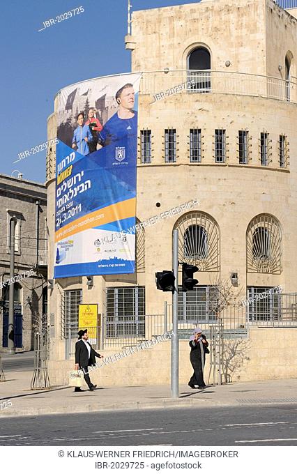 Contrast of modern advertising posters and Orthodox Jews at the corner of Ha Tsanhanim and Shivtei Israel, Jerusalem, Israel, Middle East