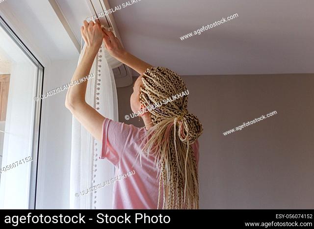 Young blonde woman hanging up curtains at the window