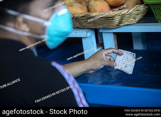 03 April 2020, Peru, Lima: A man wearing a face mask against the spread of the coronavirus holds a shopping list in front of a market stall