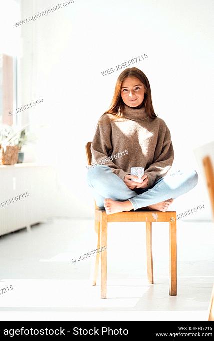 Young woman with coffee cup sitting on chair at home