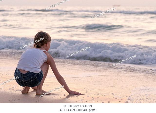 Girl playing with water on beach, rear view
