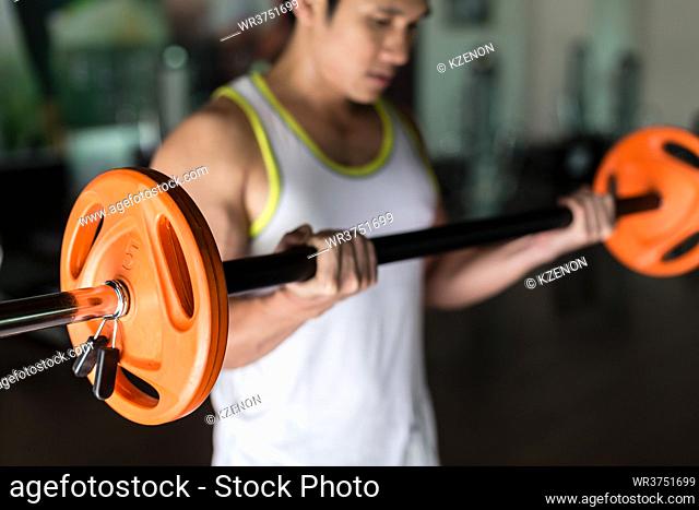Determined young man holding a barbell with supinated grip while exercising bicep curls from standing position at the gym