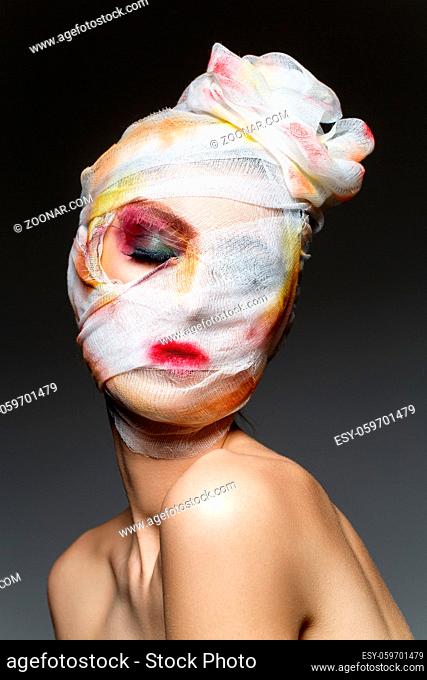 young woman with heavy makeup and bandage on head. beauty industry victim. studio shot on dark background. copy space