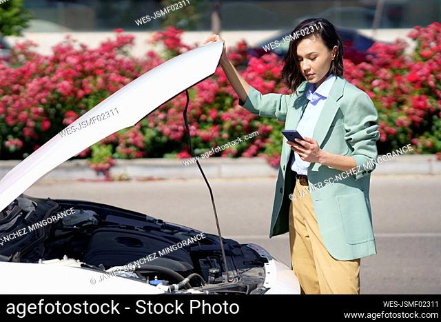 Businesswoman using smart phone while standing near broken down car