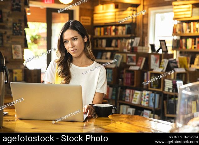 Portrait of young woman sitting at counter of coffee shop bookstore using laptop computer