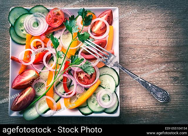 Salad of fresh vegetables on a white square plate. Vegetable still life. View from above. The concept of healthy natural food