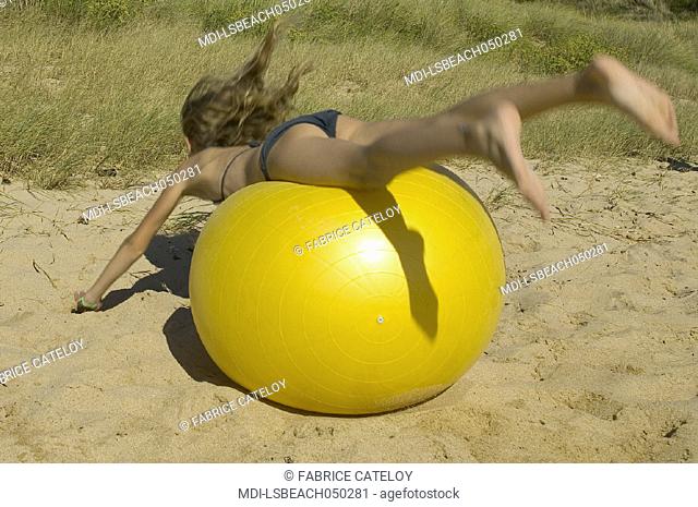 Young girl playing with a big yellow balloon on the sand beach