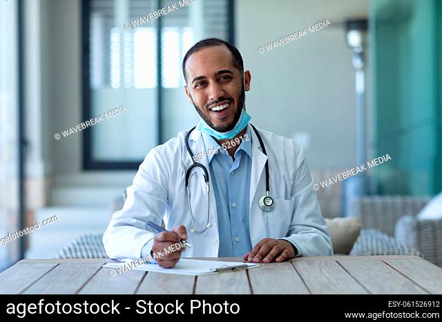 Portrait of mixed race male doctor wearing face mask looking at the camera and smiling