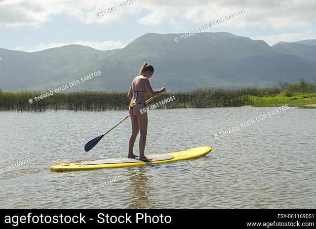Young woman practicing Stand Up Paddle on lake, yellow board, paddling. Paddleboarding