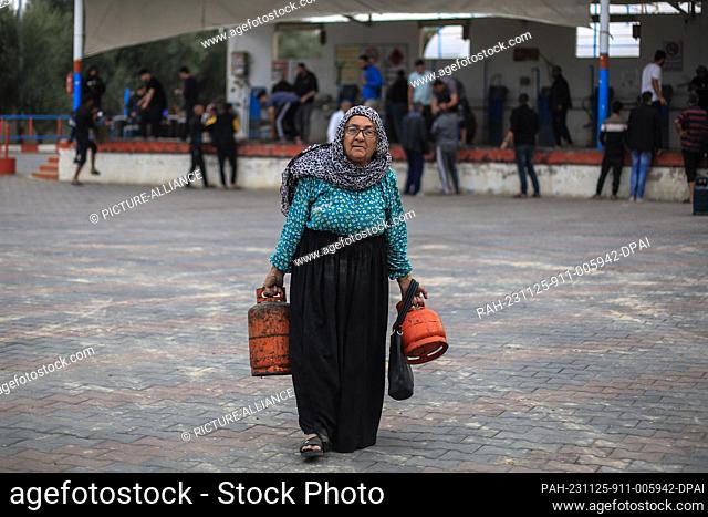 25 November 2023, Palestinian Territories, Khan Yunis: A Palestinian elderly woman carries her liquid gas cylinders after refilling them