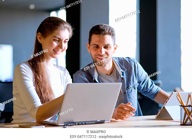 Young Smiling Coworkers Woman and Man Discusing Working Details and Pointing at Laptop Screen in Office