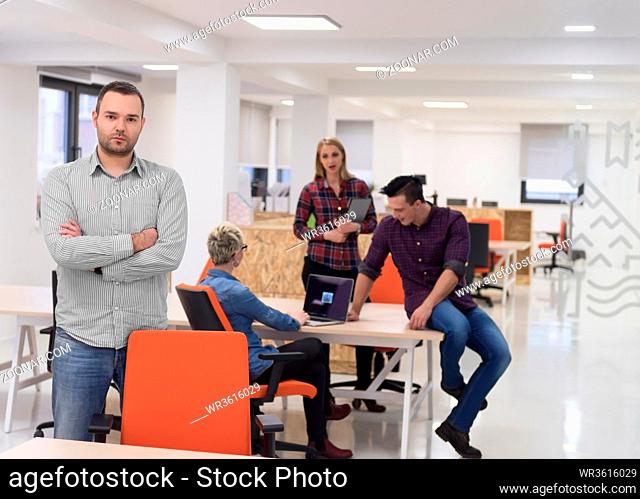 portrait of young businessman in casual clothes at modern startup business office space, team of people working together in background
