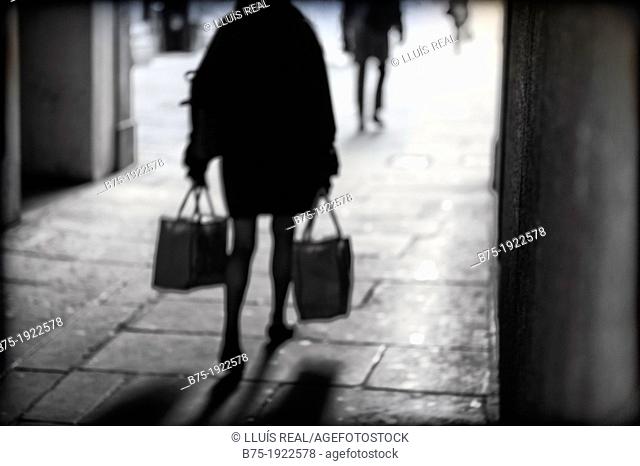 silhouette of lady walking back down the street with bags in hand