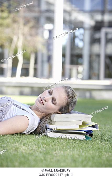Teenage girl laying down in grass on books