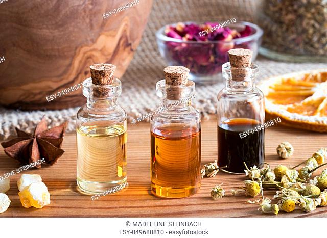 Bottles of essential oil with star anise, frankincense, dried chamomile flowers and dried orange slices