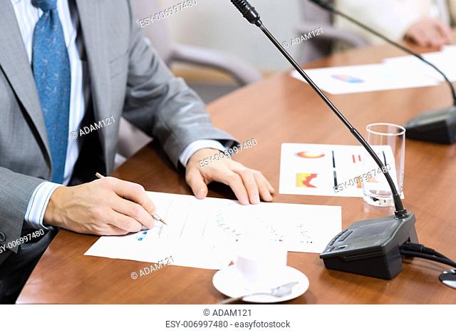 Businessman writing on paper notes, On the table is a cup of coffee and a device for communication at the conference