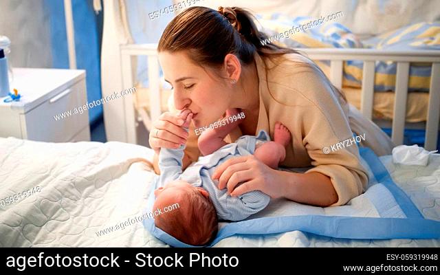 Beautiful smiling mother kissing and looking at her little baby son lying on bed at night. Happy parenting and family happiness