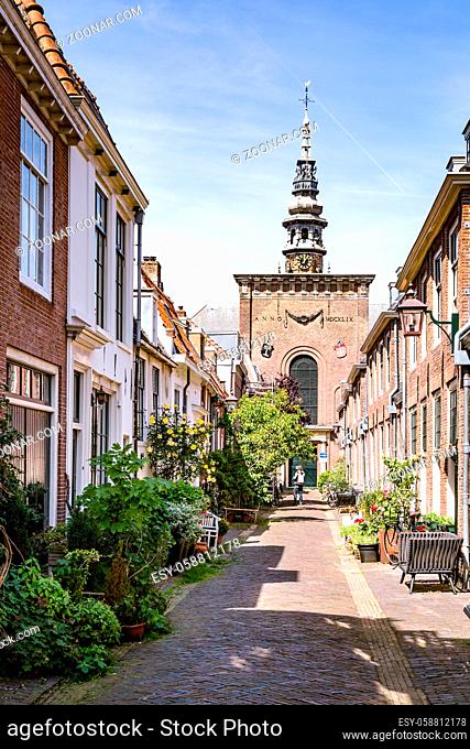 Haarlem, The Netherlands - May 31, 2019: Cozy green little street with lots of pots and plants in Haarlem with the Nieuwe kerk in the background