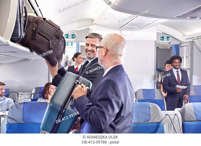 Businessmen loading luggage into storage compartment on airplane