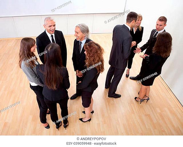High angle view of professional business people standing around in informal groups chatting as they wait for a meeting