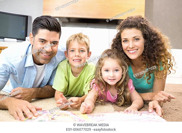 Happy siblings lying on the rug reading storybook with their parents