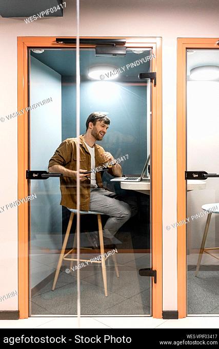 Male professional talking on video call through laptop seen through glass door in office