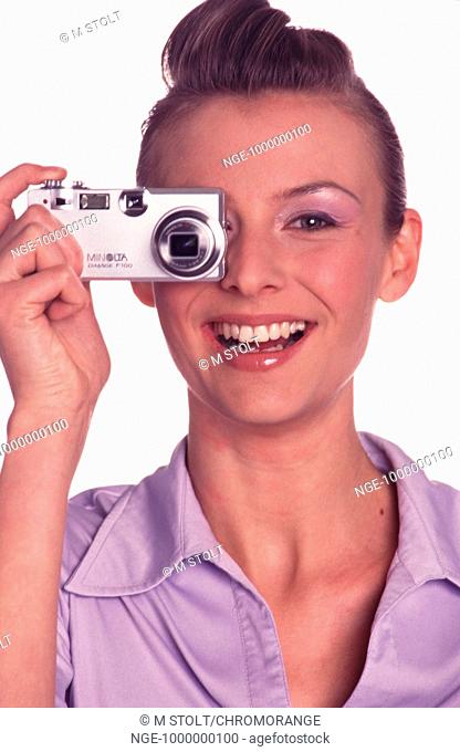 Portrait of a smiling young woman clothed with a violet blouse holding with the right hand a small camera in front of he