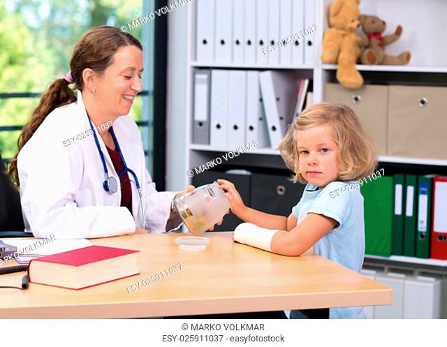 female pediatrician in white lab coat bandaging the arm of a little girl