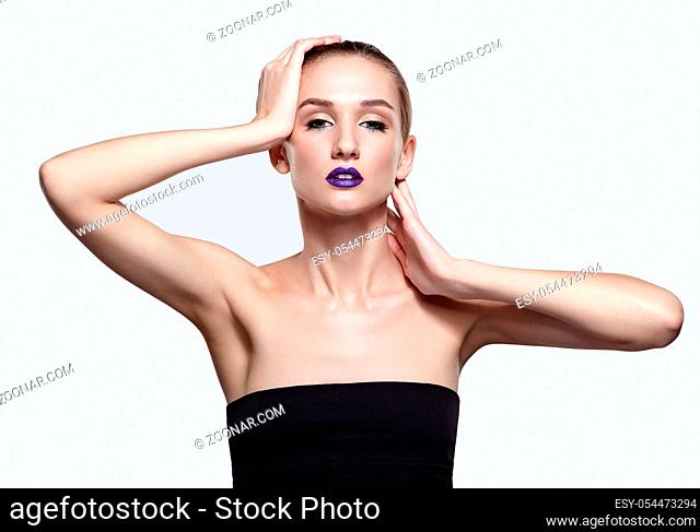 Beauty portrait of young woman with violet lips makeup. Female with hand near face on gray background