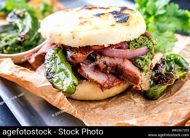 Traditional Columbian arepa con carne desmechada with shredded beef steak and aji criollo as closeup on a backing paper