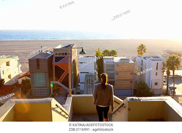 One woman leaves Palisades Park on sunny afternoon, with modern architecture beachfront homes and Pacific Ocean in distance, Santa Monica, City of Los Angeles