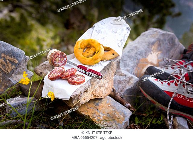 Picnic with sausage and bread rings on a stone placed beside mountaineer's shoes