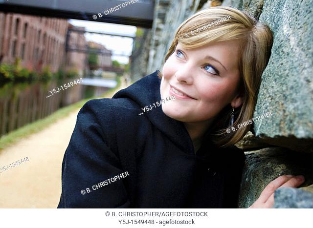Happily smiling young Caucasian female leaning on stone wall