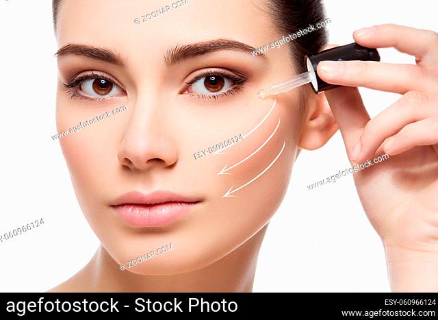Beautiful young woman applying serum moisturizer on under eye area. Beauty shot. Close-up. Direction arrows. Isolated over white background