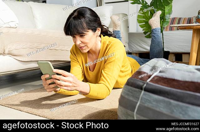 Mature woman using smart phone while lying on floor at home