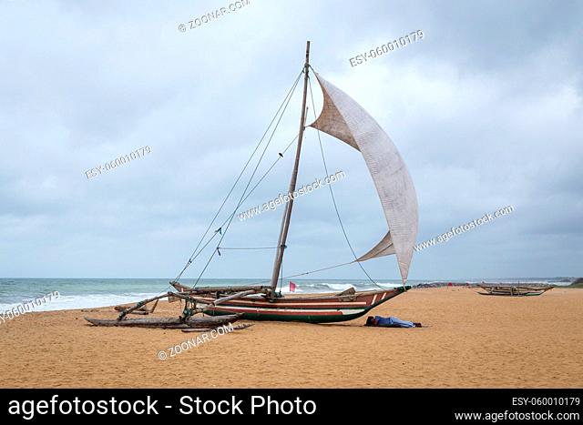 Negombo, Sri Lanka - July 25, 2018: Man sleeping next to a traditional catamaran fishing boat on the beach