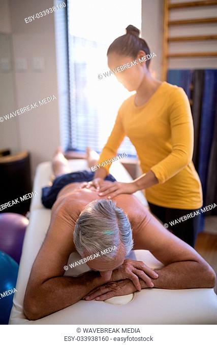 Female therapist massaging back of senior male patient against window