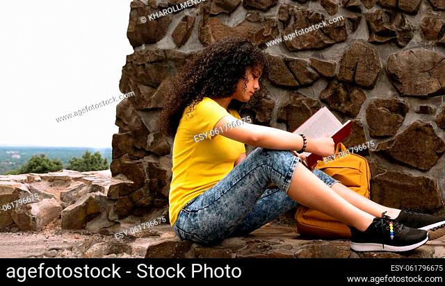 Young teenager girl reading a book and enjoying the great outdoors sitting on a rock in nature