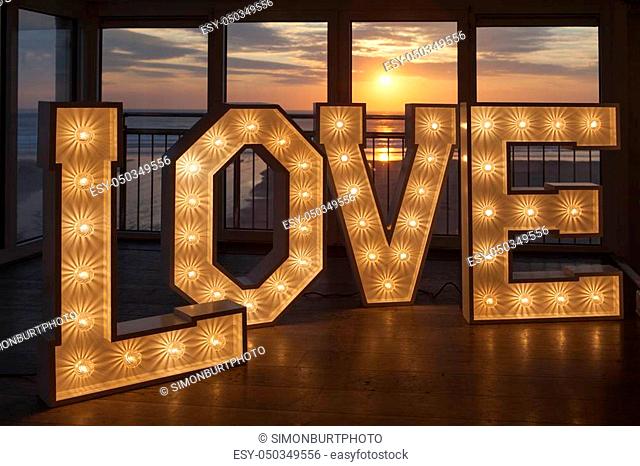 LOVE in one metre high letters lit with light bulbs at sunset at Fifteen restaurant Watergate Bay Cornwall