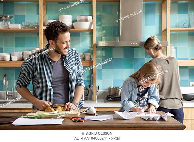 Young daughter drawing ar kitchen counter while parents prepare meal