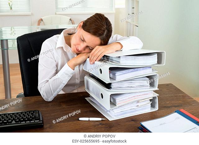 Tired Young Businesswoman Sleeping On Pile Of Folders In Office
