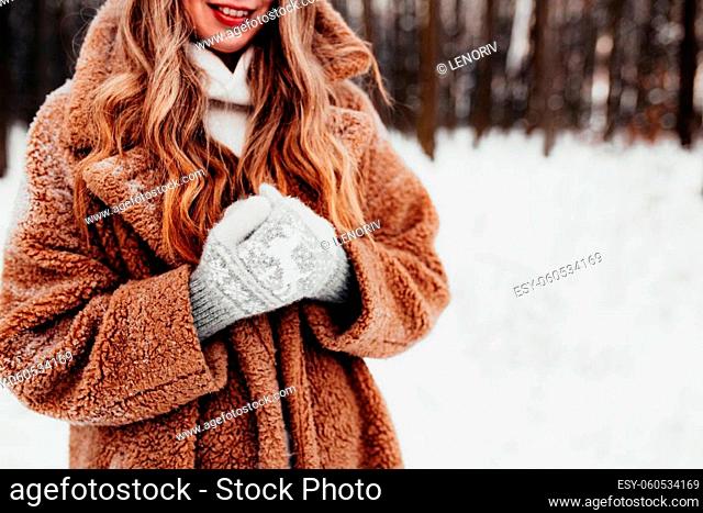 Beautiful young woman in snowy fancy winter woodland. Girl wearing fluffy gloves, cap and coat. Christmas forest, trees on blurred background